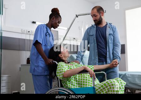 afroamerikanische Krankenschwester, die schwangere Frau im Rollstuhl in den Kreißsaal transportiert. Patientin mit Babybrücke, die sich auf die Geburt vorbereitet, während sie von ihrem Ehemann auf der Krankenstation getröstet wird Stockfoto