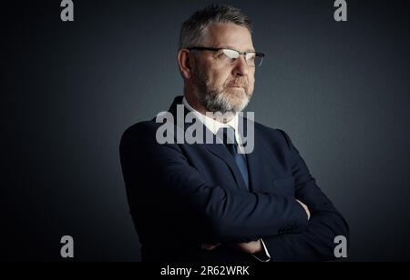 Er hat alle Optionen sorgfältig abgewogen. Studioaufnahme eines gutaussehenden, erwachsenen Geschäftsmanns, der aufmerksam aussieht, während er mit umgeklappten Armen steht Stockfoto