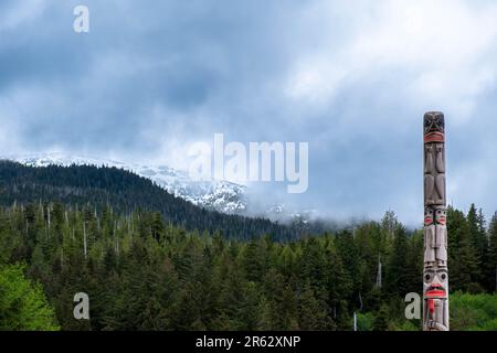 Ketchikan, Alaska, USA -21. Mai 2022: Handgeschnitzter Totem Pole und schneebedeckter Kamm im Ketchikan Heritage Totem Pole Center Stockfoto