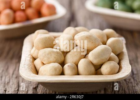 Knusprige Erdnüsse oder Cracker-Nüsse im japanischen Stil in einer kleinen Einwegschüssel mit Palmenblatt (sehr geringe Feldtiefe) Stockfoto