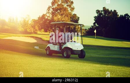 Fahren, wo das Gras grüner ist. Zwei Golfer, die in einem Wagen auf einem Golfplatz reiten. Stockfoto