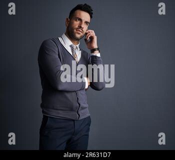 Lassen Sie es geschehen. Studioaufnahme eines stilvollen jungen Geschäftsmanns, der ein Mobiltelefon vor grauem Hintergrund benutzt. Stockfoto