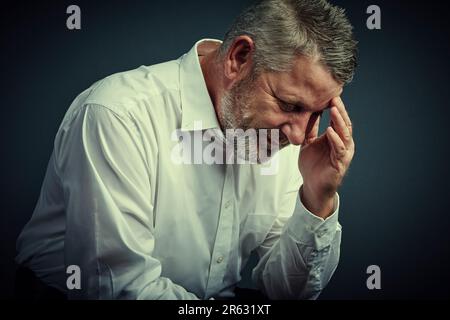 Die Spannung steigt. Studioaufnahme eines erwachsenen Geschäftsmanns, der gestresst aussieht, während er vor einem dunklen Hintergrund sitzt. Stockfoto
