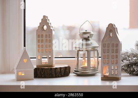 Wunderschöne Kerzenhalter in Hausform und Weihnachtsdekor auf Fensterbank im Innenbereich Stockfoto