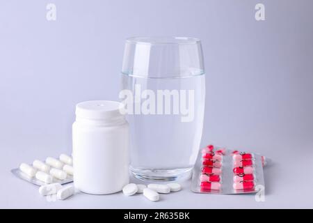 Verschiedene Antidepressiva, Medizingefäß und Glas Wasser auf hellgrauem Hintergrund Stockfoto