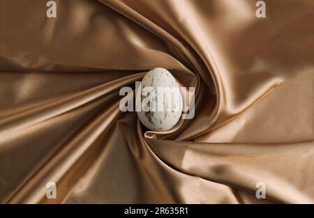 Weißes Osterei auf goldenem Seidenhintergrund. Luxuriöse Texturidee. Minimale Zusammensetzung der Osterferien. Draufsicht, flach liegend. Stockfoto