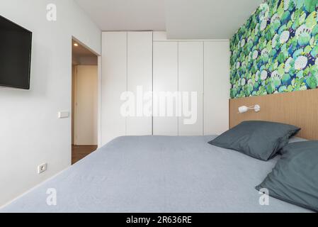 Ein Schlafzimmer mit einem Doppelbett, Fernseher an der Wand und ein Kleiderschrank mit fünf weißen Holztüren Stockfoto