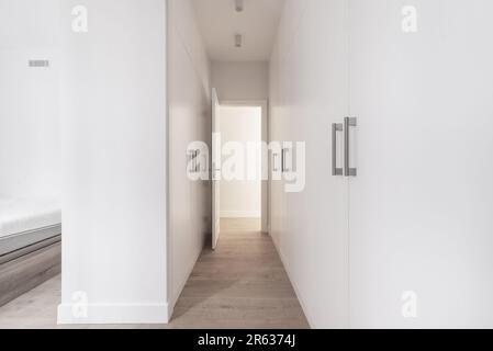 Ein begehbarer Schrank mit weißen Holztürenschränken auf beiden Seiten und einem Holzboden mit einer offenen weißen Tür Stockfoto