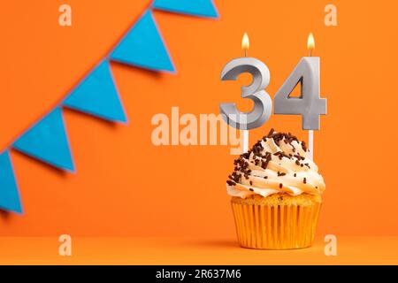 Geburtstagskuchen mit Kerze Nummer 34 - orangefarbener Hintergrund Stockfoto