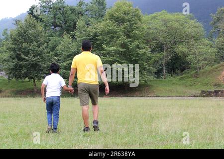 Geschiedener alleinerziehender Vater und 9-jähriger Sohn, braunhaariger Latino, wandern durch die Landschaft und schauen Hand in Hand in Hand in die Zukunft Stockfoto