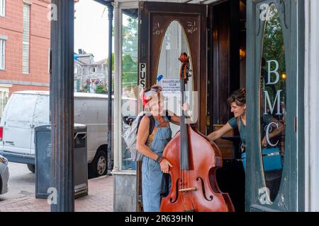 NEW ORLEANS, LA, USA - 23. APRIL 2023: Eine Bassspielerin verlässt die Vordertür des Balcony Music Clubs, während ein Freund die Tür offen hält Stockfoto