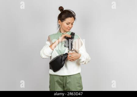 Frau mit schwarzer Ledertasche und abnehmbarer Geldbörse zum Aufbewahren von Schlüsseln, Zigaretten oder Ohrhörern am Riemen, Studio Shot Stockfoto