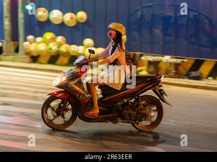 Junge vietnamesische Frau, die nachts mit ihrem Motorrad durch die Straßen von Ho-Chi-Minh-Stadt fährt. Der Hintergrund ist durch Bewegung verschwommen. Stockfoto