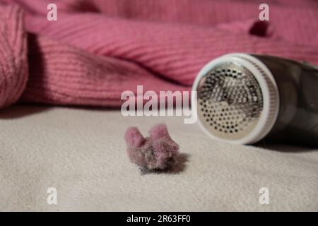 Anti-Pilling-Rasierer. Gerät zum Rasieren von Kleidung. Anti-Plush-Rasierer. Elektrischer tragbarer Pullover, Pille, Entfärbung, Fusselentferner aus pinkfarbenem Acryl- oder Wollpullover. Elektrorasierer nach der Reinigung und aufgefangenen Fusseln. Ein Pullover aus der Nahaufnahme. Alte gebrauchte Kleidung mit Pillen. Stockfoto