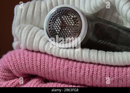 Anti-Pilling-Rasierer. Gerät zum Rasieren von Kleidung. Anti-Plush-Rasierer. Elektrischer tragbarer Pullover, Pille, Entfärbung, Fusselentferner aus pinkfarbenem Acryl- oder Wollpullover. Elektrorasierer nach der Reinigung und aufgefangenen Fusseln. Ein Pullover aus der Nahaufnahme. Alte gebrauchte Kleidung mit Pillen. Stockfoto