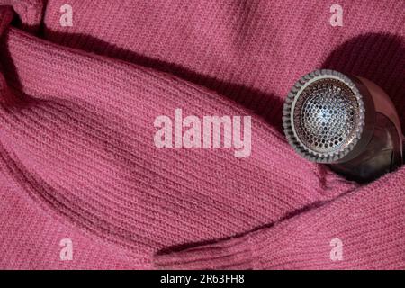 Anti-Pilling-Rasierer. Gerät zum Rasieren von Kleidung. Anti-Plush-Rasierer. Elektrischer tragbarer Pullover, Pille, Entfärbung, Fusselentferner aus pinkfarbenem Acryl- oder Wollpullover. Elektrorasierer nach der Reinigung und aufgefangenen Fusseln. Ein Pullover aus der Nahaufnahme. Alte gebrauchte Kleidung mit Pillen. Stockfoto
