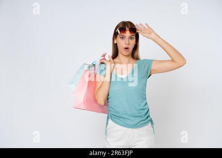 Eine glückliche junge Frau, die eine Sonnenbrille trägt und Einkaufstaschen isoliert auf weißem Hintergrund hält. Stockfoto