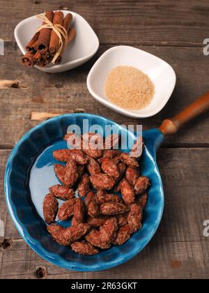 Schmackhafte geröstete Mandeln in einer blauen Keramikschale mit Zutaten auf Holz Stockfoto