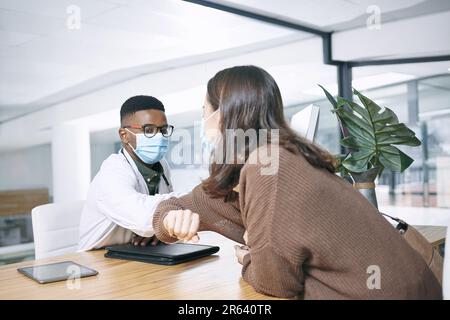 Wir sorgen dafür, dass wir in meiner Klinik soziale Distanz wahren. Ein junger Arzt, der bei seiner Patientin sitzt und sie mit einer Ellenbogenversteifung in der Klinik begrüßt. Stockfoto
