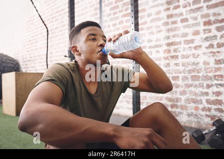 Ohne Wasser können wir nicht leben. Ein sportlicher junger Mann, der eine Flasche Wasser im Fitnessstudio trinkt. Stockfoto