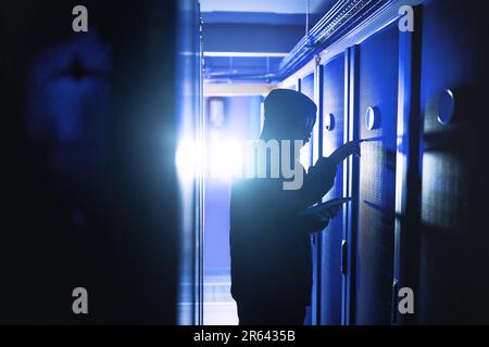 Es ist so einfach, dass Systeme beschädigt werden. Ein Hacker, der ein digitales Tablet in einem Serverraum verwendet. Stockfoto
