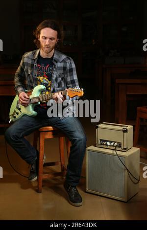 Bärtiger Gitarrist, der eine E-Gitarre mit einem Verstärker spielt Stockfoto