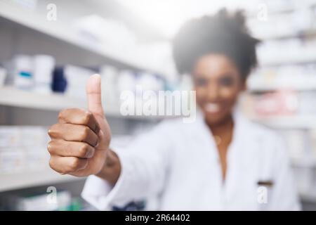 Vom Apotheker zugelassen. Ein selbstbewusster junger Apotheker, der in einer Apotheke Daumen hoch zeigt. Stockfoto