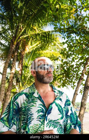 Vertikales Porträt eines Mannes mit Hawaiianischem Hemd und Sonnenbrille neben einer Palme Stockfoto