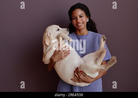 Porträt einer schwarzen jungen Frau, die den Hund hält und vor der Kamera lächelt Stockfoto