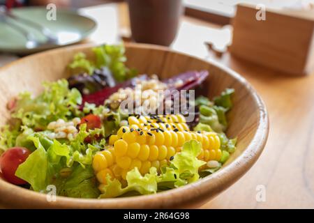 Frisches Gemüse und Obstsalat mit Mais, Rote Bete, Hirse, Salat, Tomaten in einer Holzschüssel auf einem Holztisch. Stockfoto