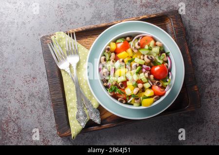 Hausgemachter frischer Salat mit rohem Gemüse und gekochten schwarzen Erbsen aus nächster Nähe in einer Schüssel auf einem Holzbrett. Horizontale Draufsicht von oben Stockfoto