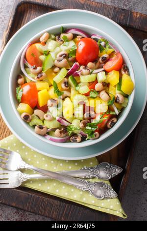 Frischer Schwarzaugensalat mit Tomaten, Sellerie, Pfeffer, Gurke und Zwiebeln in einer Schüssel auf dem Tisch. Vertikale Draufsicht von oben Stockfoto