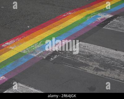 Ein lebendiges Regenbogengemälde ist an der Seite einer Straße gemalt und verleiht der ansonsten einfachen Landschaft einen Farbschub Stockfoto