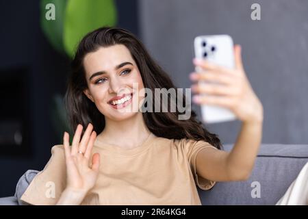 Frau, die zu Hause bei einem Videoanruf über ein Smartphone winkt Stockfoto