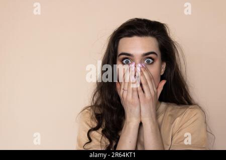 Verwirrte Frau reagiert auf etwas mit wunderbarem, verängstigtem Ausdruck über beigefarbener Wand Stockfoto