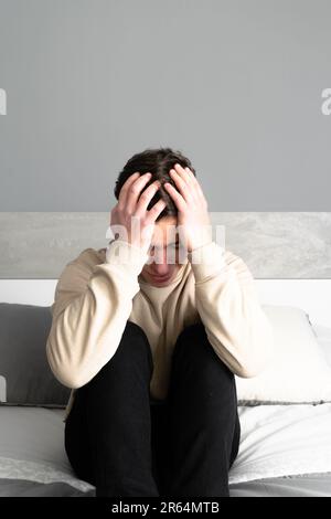 Ein trauriger junger Mann klagt, auf seinem Bett zu sitzen Stockfoto