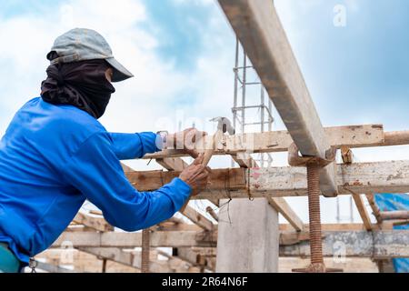 Arbeiter schlug Nagel auf Holzstäbchen für Stützgerüst auf Baustelle. Stockfoto