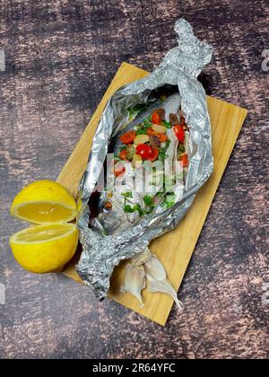 Goldbrasse en Papillote mit Kirschtomaten, Knoblauch und Kapern bereit zum Kochen im Ofen Stockfoto