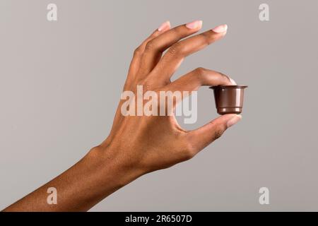 Nicht wiedererkennbare afroamerikanische Frau, die Kaffeekapsel vor grauem Hintergrund im hellen Studio vorführt Stockfoto