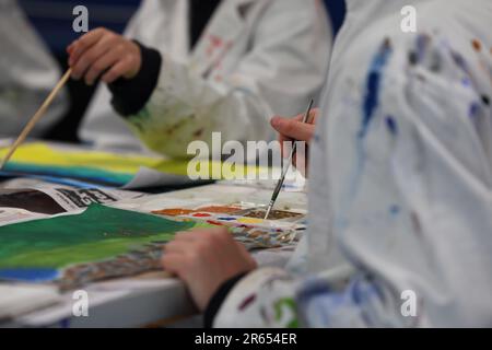 Studenten der bildenden Kunst tragen befleckte weiße Kittel oder Schürzen, die Farben auf einer Farbpalette für ein Kunstwerk oder Malprojekt mischen. Kunstunterricht im Handumdrehen Stockfoto