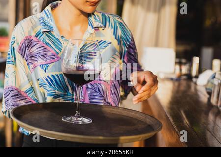 Kellnerin serviert ein Glas Rotwein auf einem Tablett. Stockfoto