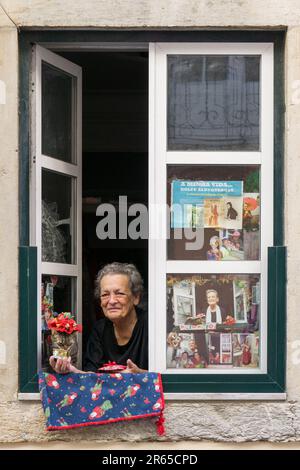 Lissabon, Portugal. 10.05.2023. Eine berühmte ältere Einwohnerin von Lissabon sitzt am Fenster mit ihrer Katze im Hut. Portugal Stockfoto