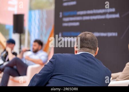 Rückansicht eines unbekannten Mannes im formellen Anzug, der während des Saalgesprächs auf einer verschwommenen Bühne sitzt und den Vorträgen der Referenten zuhört Stockfoto