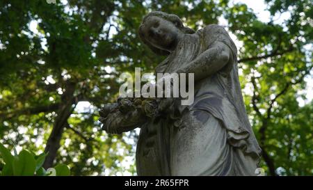 Skulptur einer schönen Frau auf einem Friedhof/Friedhof. Sie hat einen wreth in der Hand. Stockfoto