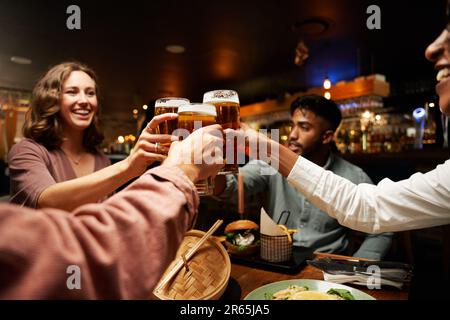 Fröhliche, junge, multiethnische Gruppe von Freunden in legerer Kleidung, die in der Bar Toast mit Bier trinken Stockfoto
