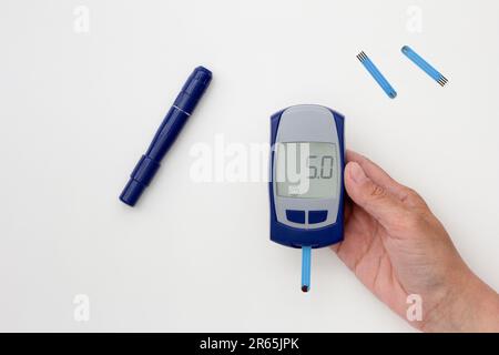 Draufsicht der zugeschnittenen Frau Hand, die das Glukometer mit 5,0 Ergebnis auf der Anzeige hält, mit Blutteststreifen innen, Lanzette und Teststreifen auf weißem Hintergrund Stockfoto