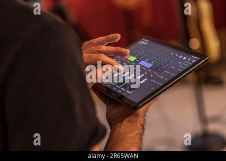 Ein erfahrener Toningenieur verwendet ein Tablet zur Feinabstimmung der Audiopegel während einer dynamischen Live-Konzert-Vorstellung. Stockfoto