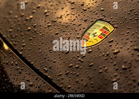 Masi, Italien, 7. juni 2023: Nahaufnahme eines schwarzen Autos mit dem berühmten Porsche-Emblem und Wassertropfen. Stockfoto