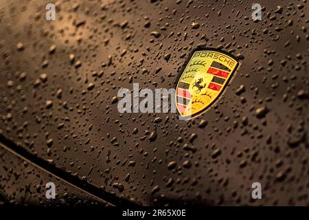 Masi, Italien, 7. juni 2023: Nahaufnahme eines schwarzen Autos mit dem berühmten Porsche-Emblem und Wassertropfen. Stockfoto