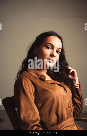 Eine junge Frau, die ein braunes Kleid trägt und auf einem Stuhl sitzt Stockfoto